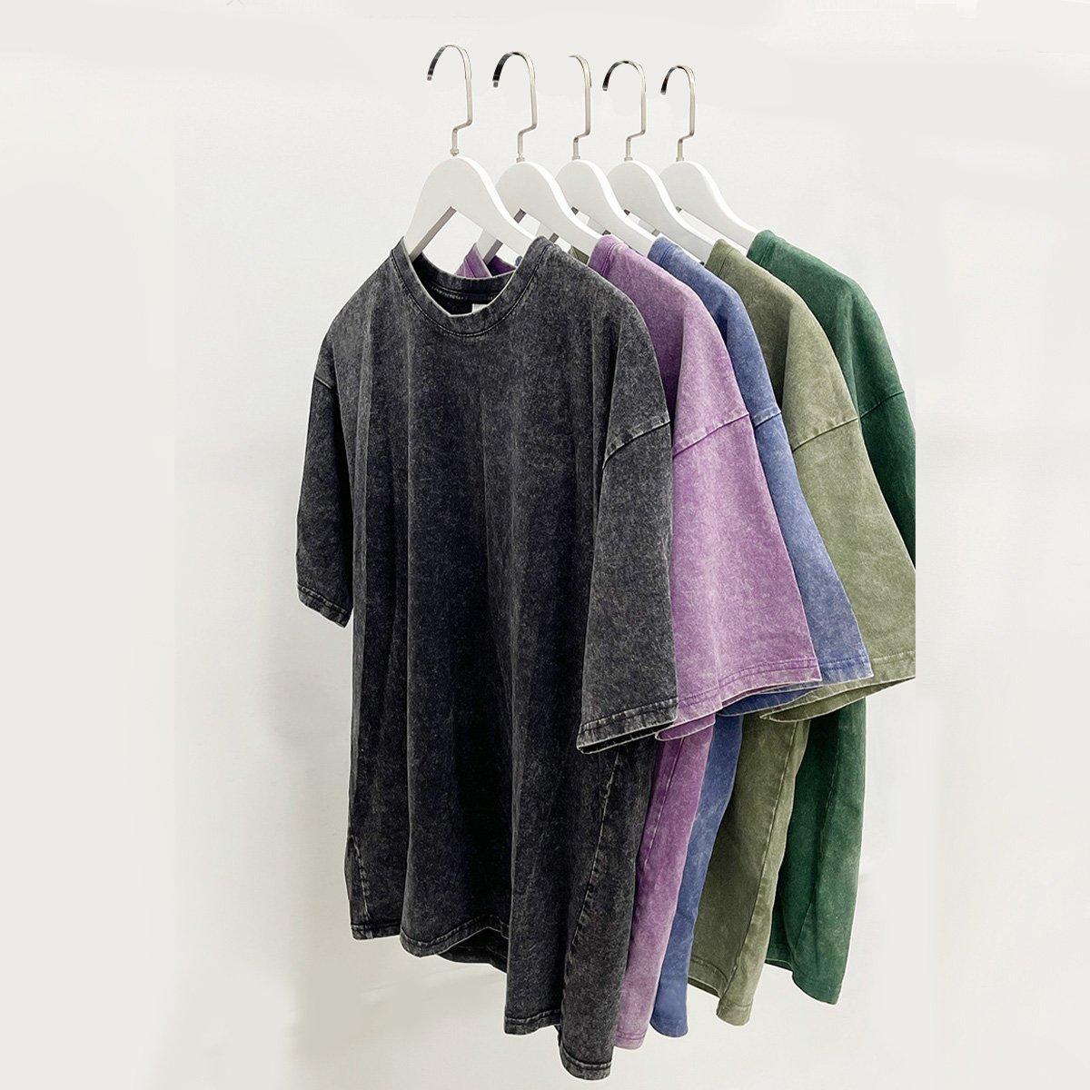 Five custom acid wash oversized cotton t-shirts in various colors hanging on hangers.