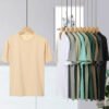 A cream t-shirt on a hanger with other t-shirts in various colors in the background.
