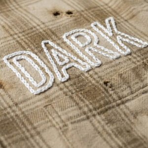 Close-up of a distressed plaid shirt with embroidered 'DARK' text.