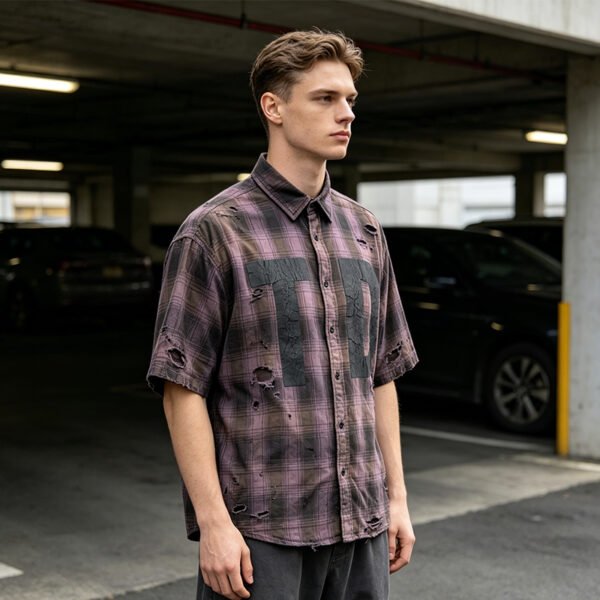 Man wearing a distressed plaid short-sleeve shirt in a parking garage.