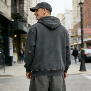 Man wearing a dark grey vintage-wash distressed zip hoodie with ripped details.