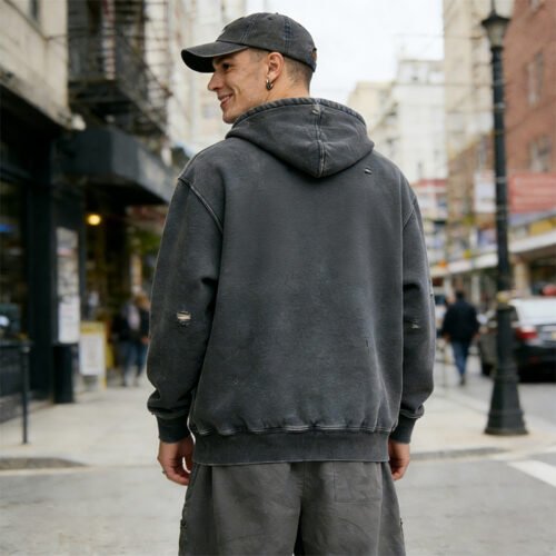 Man wearing a dark grey vintage-wash distressed zip hoodie with ripped details.