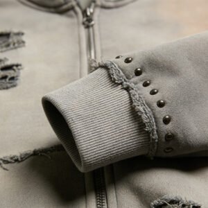 Close-up of a distressed grey zip-up hoodie sleeve with metal studs.