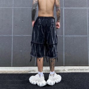 Man wearing black acid-washed denim shorts with tassels and raw hem.