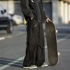 Man wearing loose black multi-pocket cargo pants with a skateboard