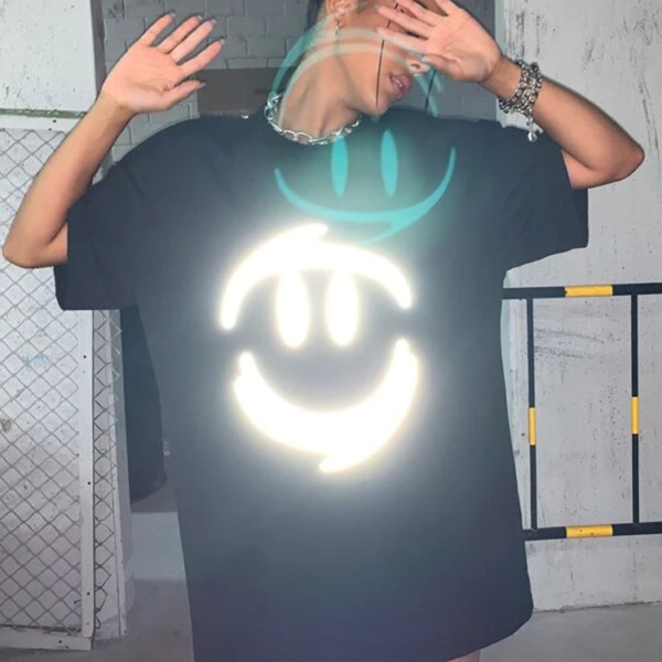 Person wearing an oversized black t-shirt with a reflective smiley face graphic