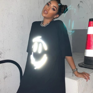 Woman wearing a black oversized t-shirt with a reflective smiley face graphic.