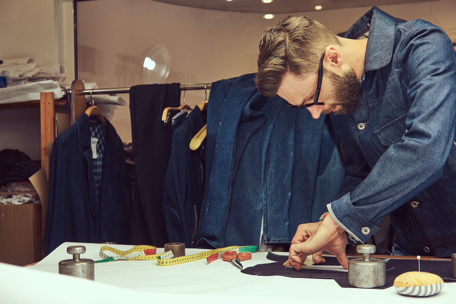 Tailor cutting fabric for a garment with a measuring tape and scissors.