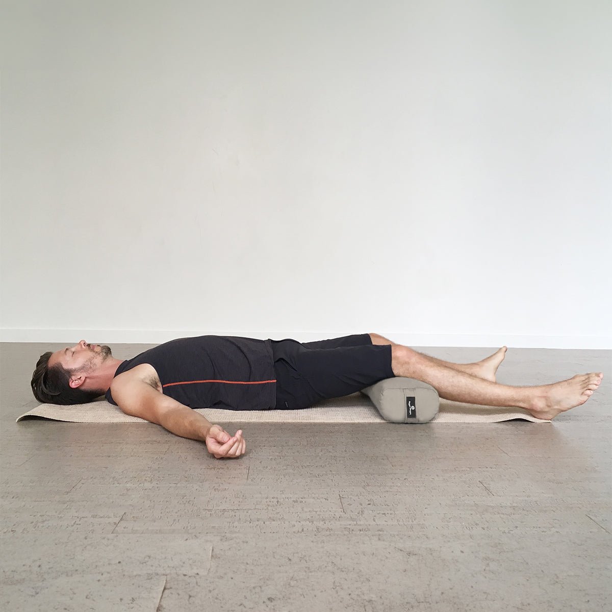 Man lying on a yoga mat with a bolster under his knees