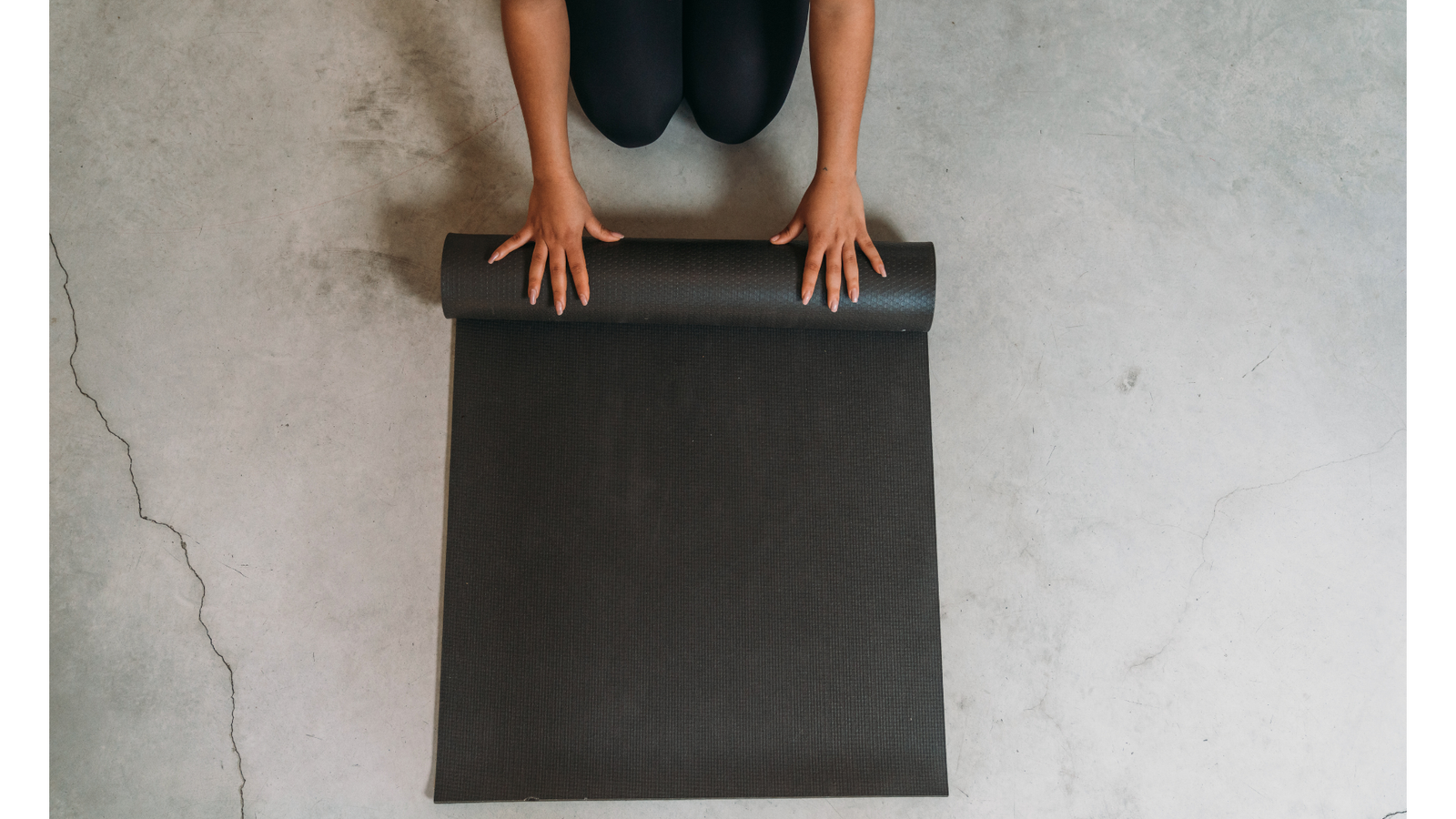 Person unrolling a black yoga mat on a concrete floor