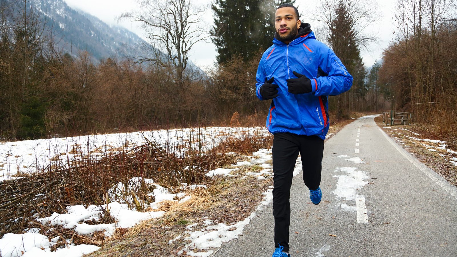 Man in blue hooded ski jacket running outdoors in winter